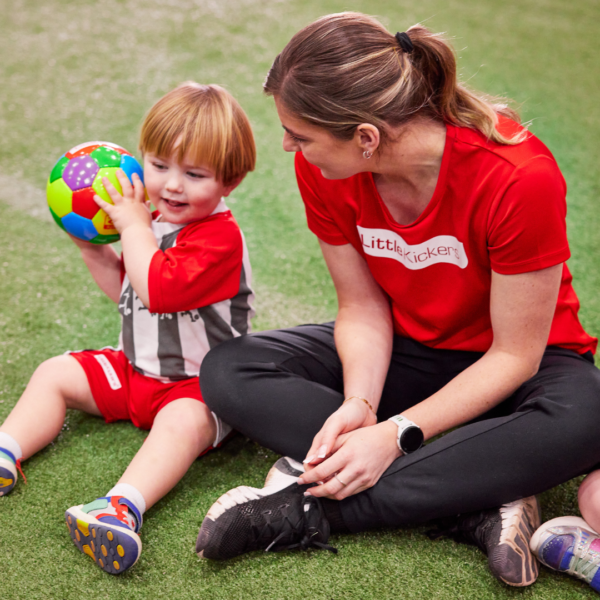 Little Kickers weekend coach playing with a young child between 1.5 to 3 years holding a multi-coloured football.